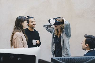 Happy computer programmer wearing vr glasses while talking to colleagues in office