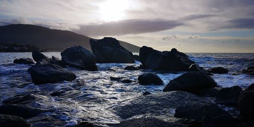 Rocks on beach against sky during sunset