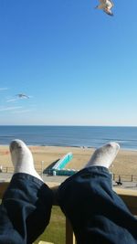 Low section of man flying over sea against clear blue sky