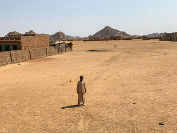 Rear view of man standing on desert against sky