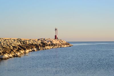 Lighthouse by sea against clear sky