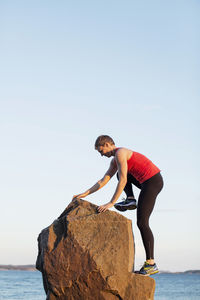 Full length of sporty woman climbing on rock against clear sky