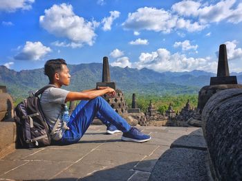 Side view of man sitting on mountain against sky