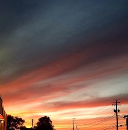 Low angle view of silhouette electricity pylon against dramatic sky