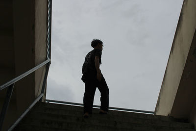 Low angle view of man standing by railing against sky