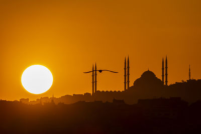 Silhouette built structures against orange sky