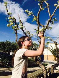 Teenage girl plucking flowers from plant at park against sky