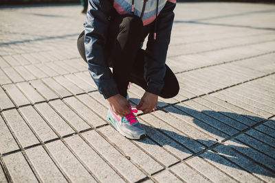 Low section of female athlete tying shoelace at footpath