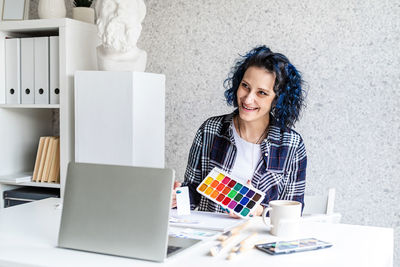 Smiling woman holding watercolor paint sitting at home