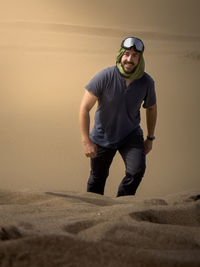 Portrait of young man standing on sand at beach during sunset