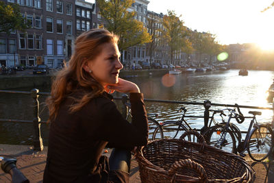 Beautiful young woman in basket against building in city at sunset