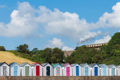 Colourful beach houses. row of  beach huts with steam train on stone viaduct against blue sky.