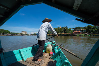 Rear view of man boating in sarawak river against sky