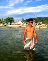 Shirtless man standing in water against sky