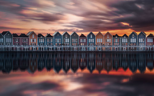 Panoramic view of houses by sea against orange sky