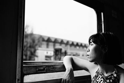 Portrait of woman looking away while sitting on window