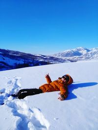 Man gesturing thumbs up sign while lying in deep snow on mountain