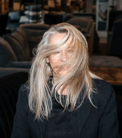 Mysterious woman with windswept silver hair in chic black attire at upscale furniture showroom