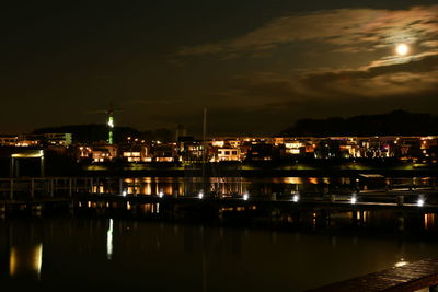 Illuminated buildings by sea against sky at night