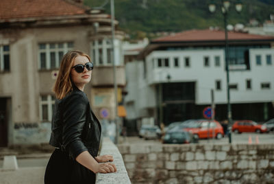 Portrait of young woman standing on bridge in city