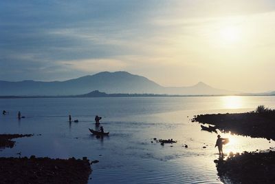 Silhouette people on lake against sky during sunset