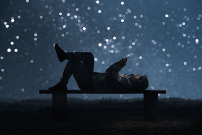 Side view of man sitting on bench at night