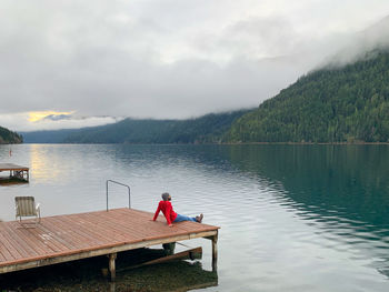 Rear view of man sitting on lake against sky