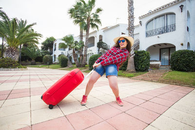 Full length portrait of young woman standing by palm trees