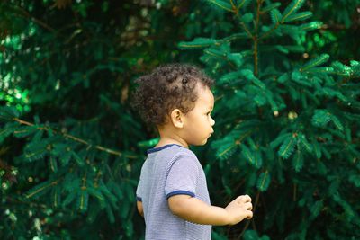 Side view of cute baby boy standing against plants