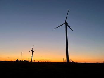 Silhouette wind turbines on field against sky during sunset