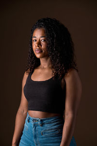 Portrait of young woman standing against black background