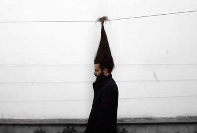 Side view of man with long hair on cable against white wall