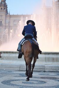 Rear view of man riding horse towards fountain