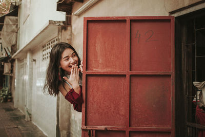 Smiling young woman hiding by door