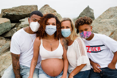 Family with masks posing on rocks at beach