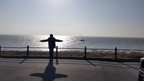 Woman with arms outstretched standing on promenade against sky