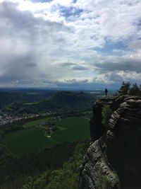 Man standing on cliff by landscape against sky