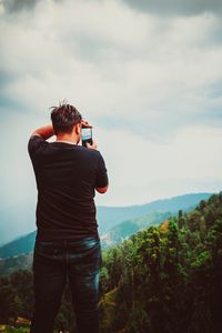 Rear view of man photographing on mountain against sky