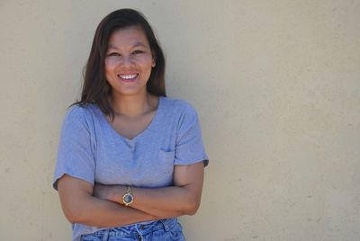 Portrait of a smiling young woman standing against wall