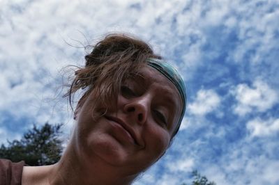 Low angle portrait of woman against cloudy sky