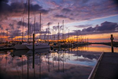 Sailboats moored in harbor against sky during sunset