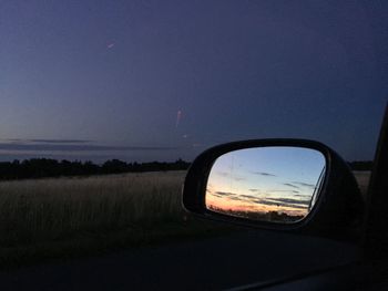 Reflection of car on side-view mirror against sky at dusk