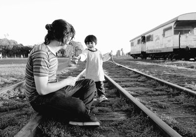 Side view of man with son walking on railroad track against clear sky