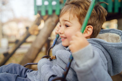 Side view of cute boy playing on swing at playground