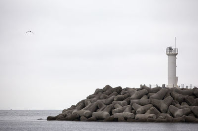 Lighthouse and tetrapods by sea against clear sky