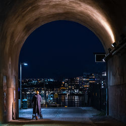 Rear view of woman pushing baby carriage on illuminated street at night