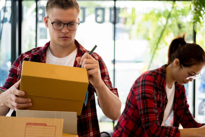 Man writing on cardboard box with female coworker in office