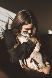 Pretty young female holding a dog while sitting on a couch in cozy room