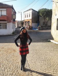 Full length portrait of young woman standing on street against building