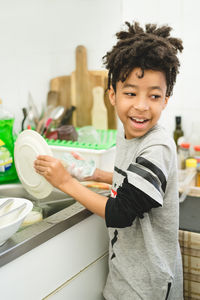 Side view of smiling boy washing dishes in kitchen